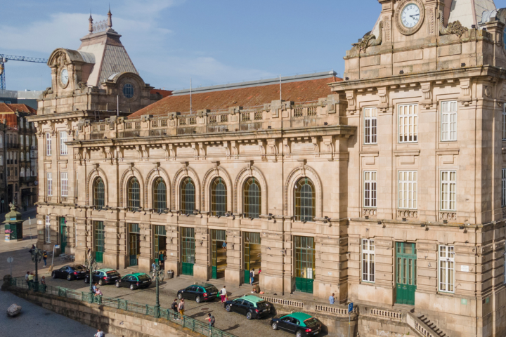 Historic train station building with large arched windows and clock towers on a sunny day.