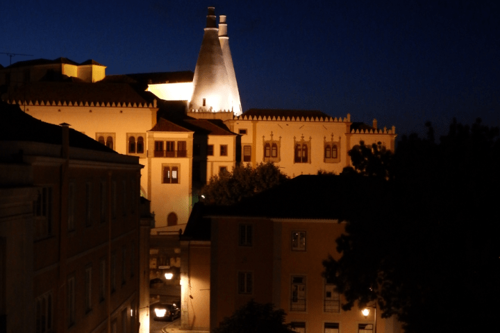 Illuminated city buildings and street at night with a deep blue sky.