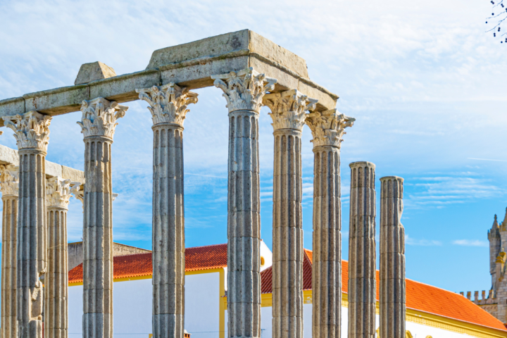 Ancient stone columns of a Roman temple against a blue sky in Évora, Portugal.