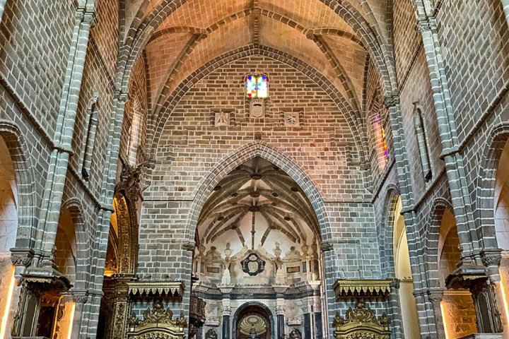 Interior of a cathedral with vaulted ceilings, arches, and ornate altarpiece.
