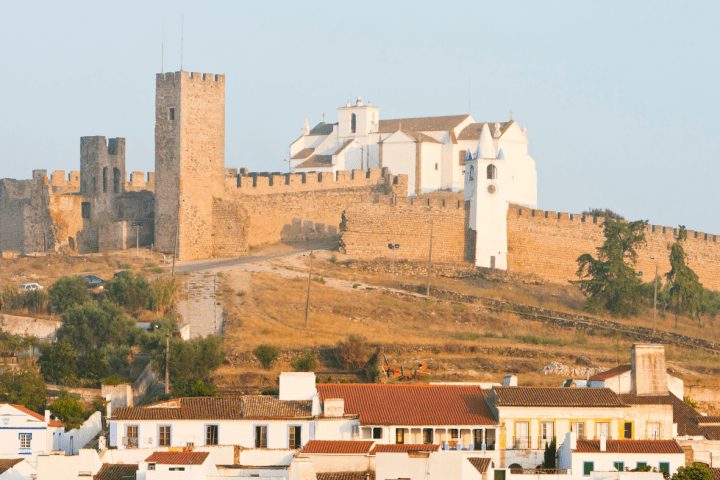 Ancient fortress with a church on a hill, surrounded by houses with red roofs.