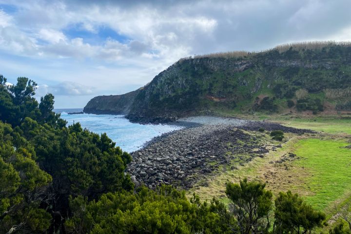 Rocky coastline with green hills, blue sky, and scattered clouds.