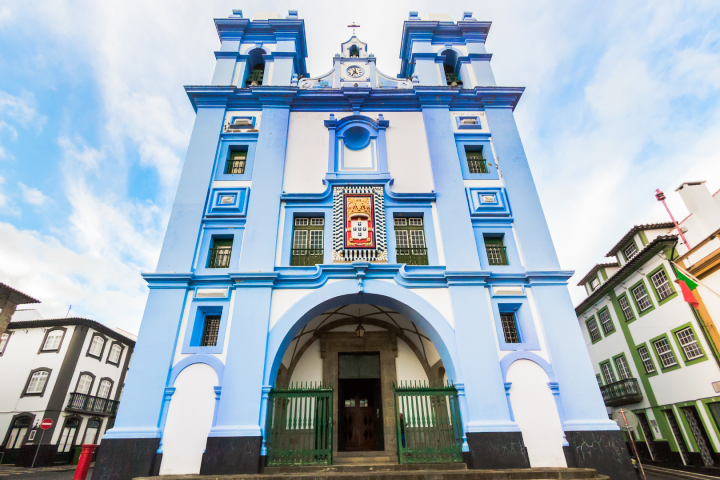 Blue and white church facade with arches and towers against a cloudy sky.