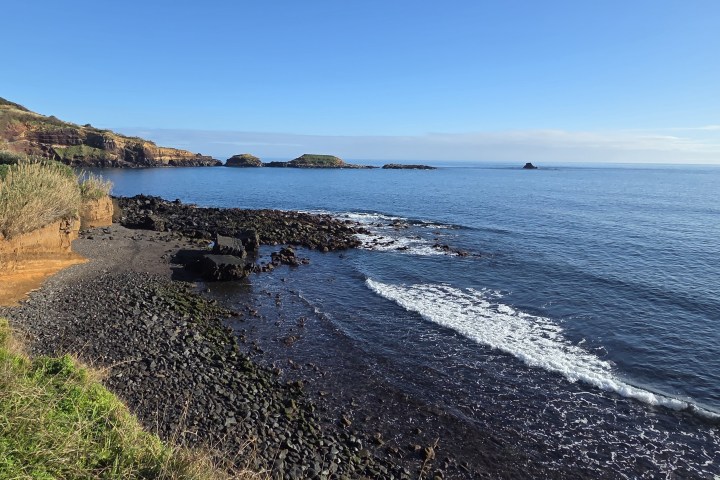 Rocky coastline with gentle ocean waves and clear blue sky.