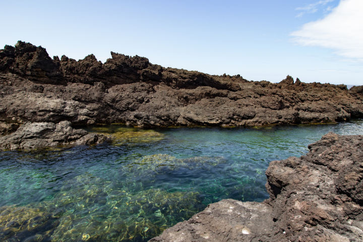 Rocky shoreline with clear blue water and a cloudy sky.