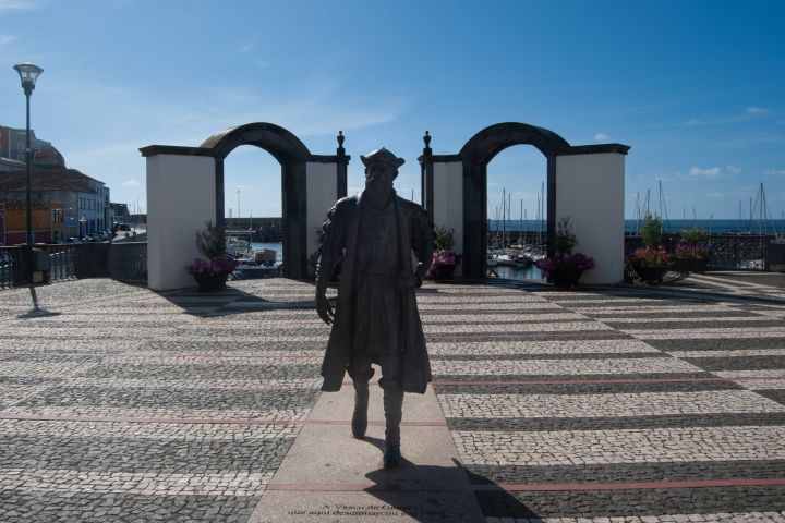 Silhouette of a statue with an archway and marina in the background under a clear blue sky.