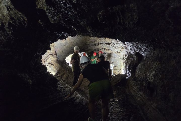 People wearing helmets exploring a dark cave tunnel made of rough rock formations.