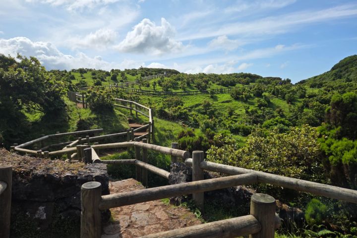 Scenic green landscape with a fenced wooden path and cloudy blue sky.