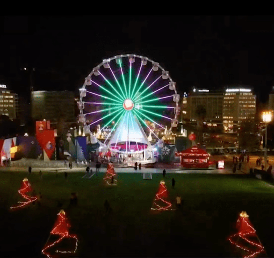 Illuminated Ferris wheel and red lit trees at night in a cityscape setting.