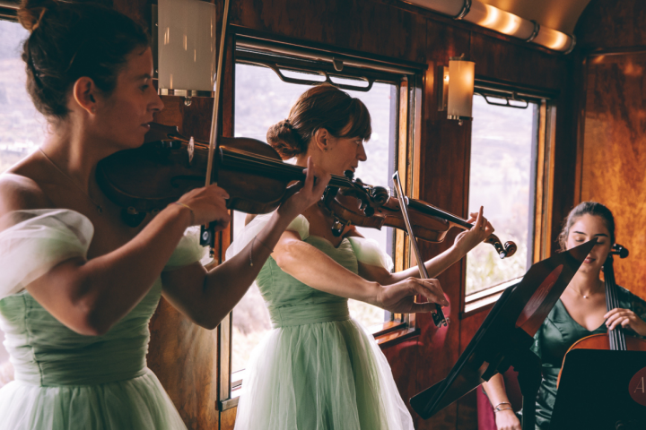 Three women in green dresses play string instruments on a vintage train.