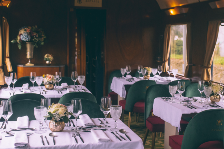 Elegant train dining car with set tables, green chairs, and flowers.