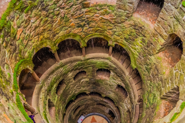 Spiral stone staircase with arches in a moss-covered well.