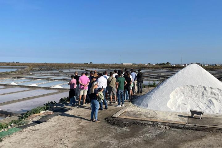 Group of people near a salt pile and flat salt pans under a clear blue sky.