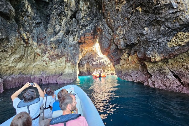 People on a boat entering a rocky sea cave with clear blue water.