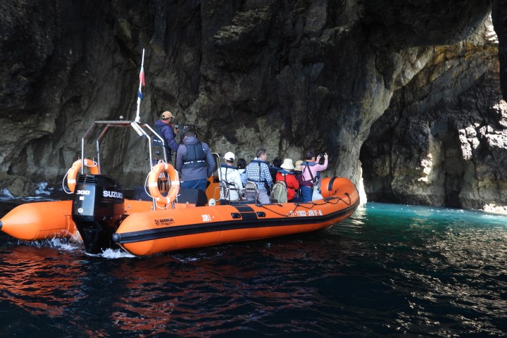 Group on an orange inflatable boat exploring a cave on the water.