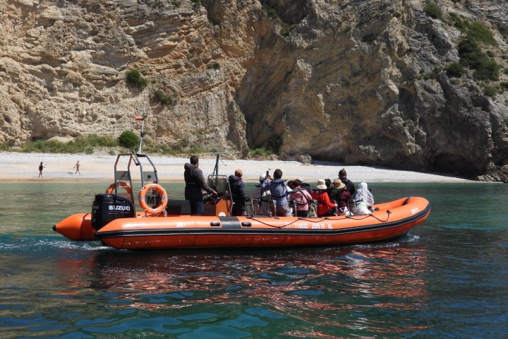 Orange inflatable boat with passengers near a rocky shore.