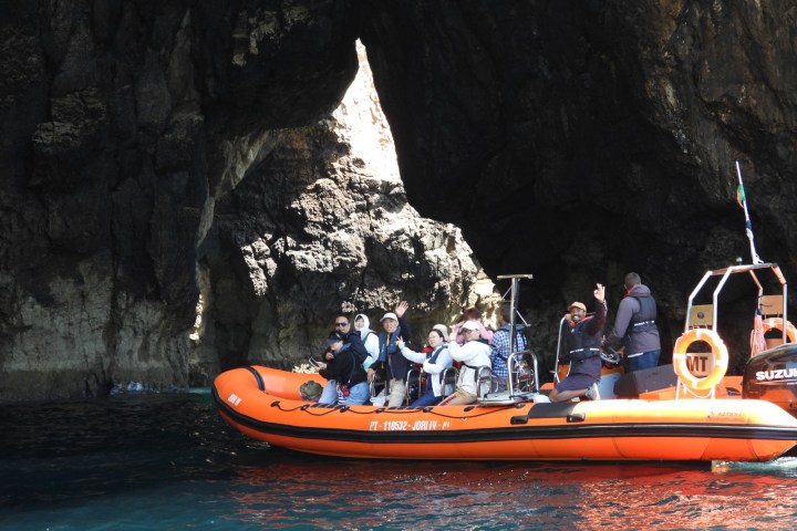 Orange boat with people, near a rocky cave on the water.