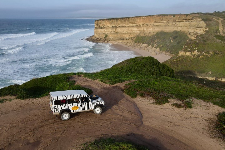 Safari jeep on a cliffside overlooking the ocean and waves.