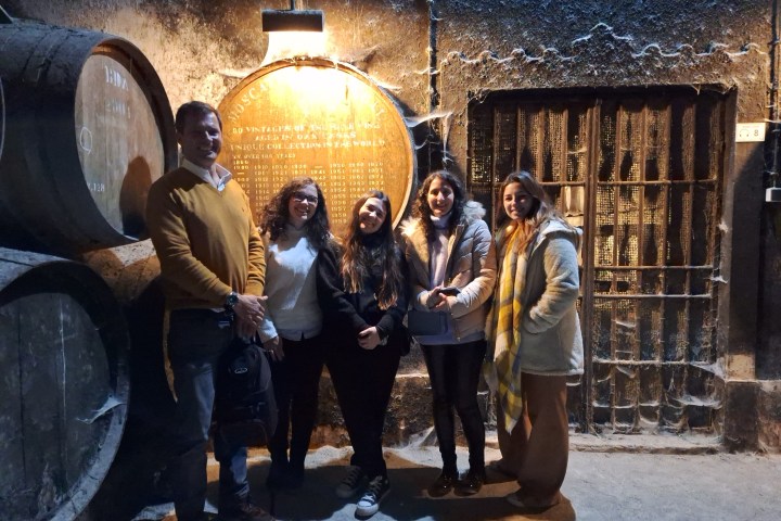 Group of people standing by barrels in a dimly lit cellar.