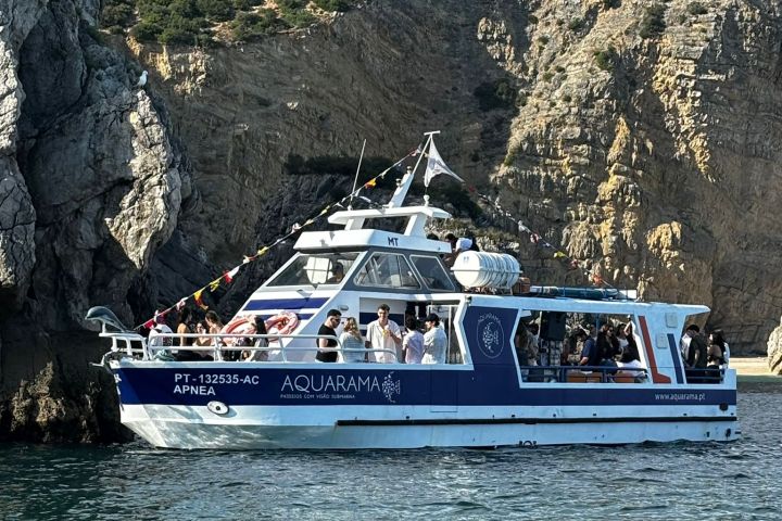 Tour boat with passengers near rocky cliffs on a sunny day.