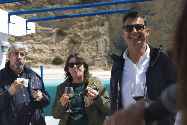 Three people enjoying wine outdoors near rocky beach scenery.