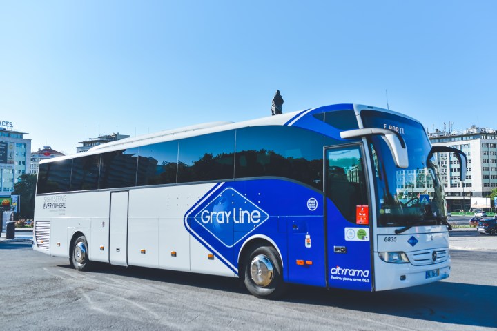 White and blue tour bus parked in a city area.
